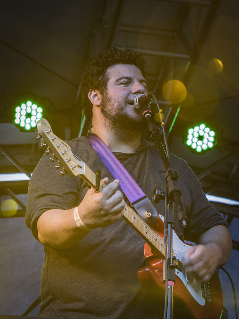 International blues guitarist singing into a microphone and playing guitar during a live performance.